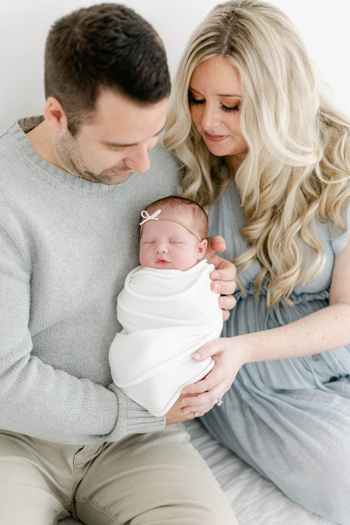 Dad and mom holding their baby girl dressed in neutral tones and cool blues for their newborn session photographed by Philadelphia Newborn Photographer Tara Federico