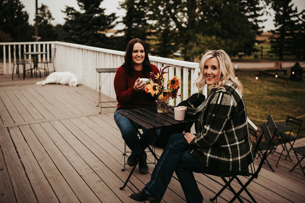 two women sitting on a porch drinking coffee