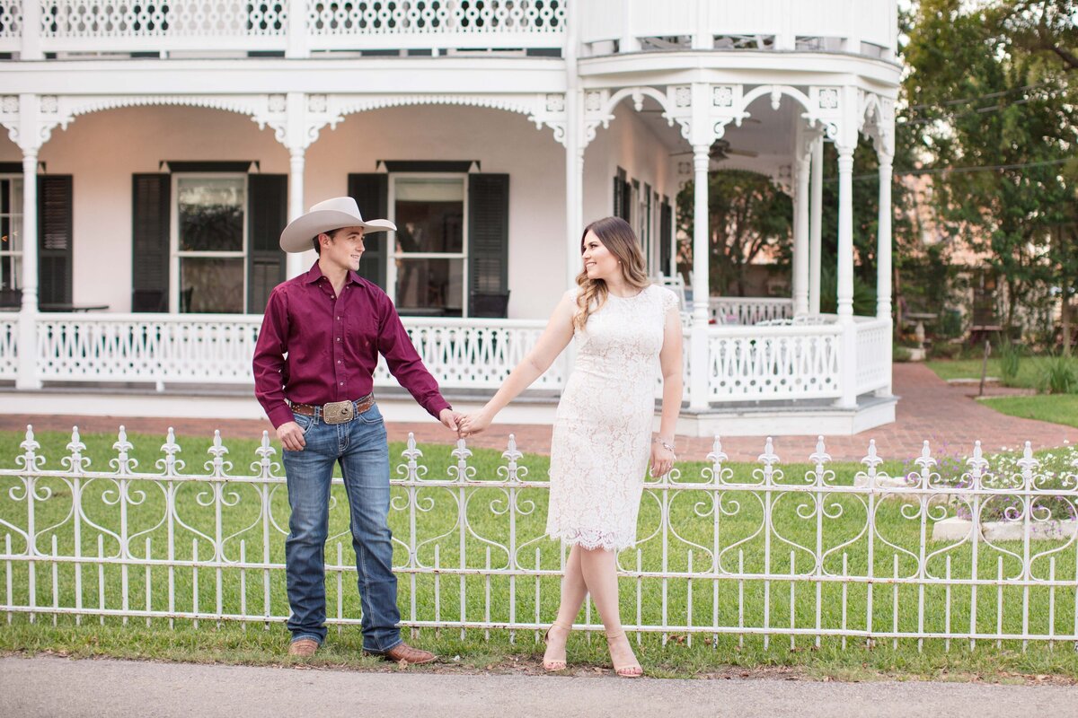 wedding engagement holding hands walking next to Gruene Mansion Inn in New Braunfels Texas historic home and iron fence by Firefly Photography