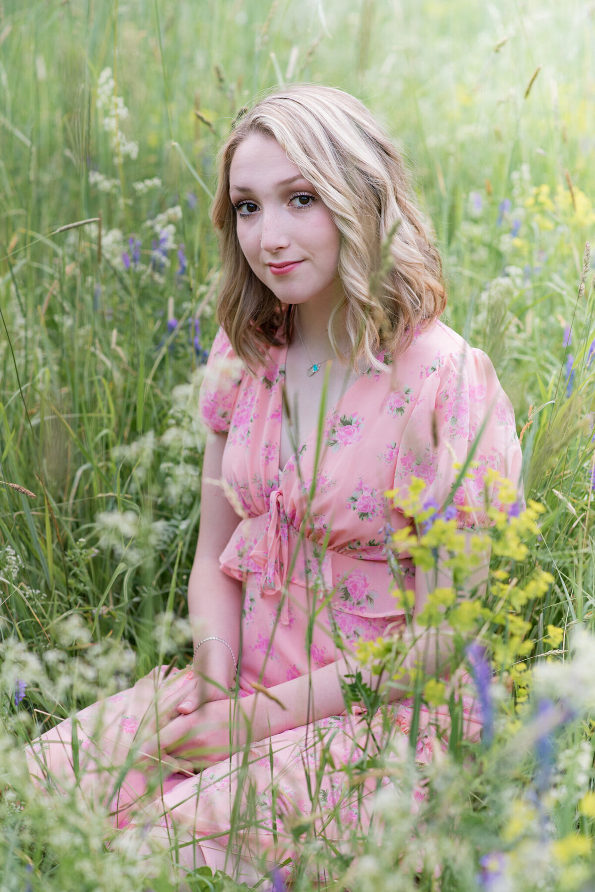 Teen girl in pink dress sitting in a field of wildflowers