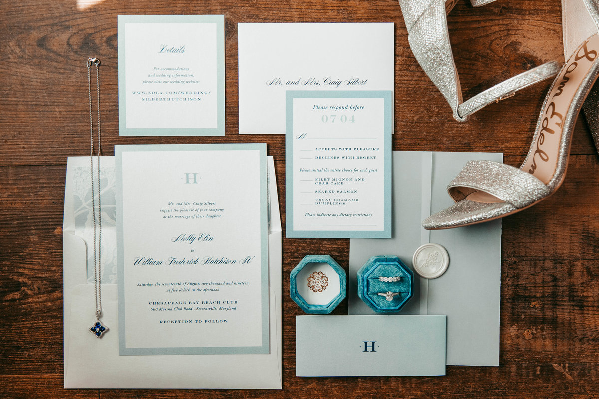 A flatlay of a bride's details on her wedding day, including the invitations, her shoes, rings, and a necklace