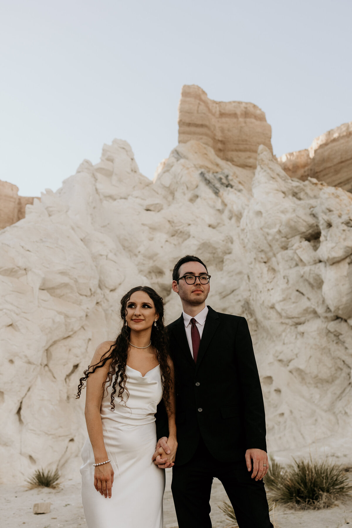 portrait of a bride and groom standing together in front of a massive white rock in New Mexico