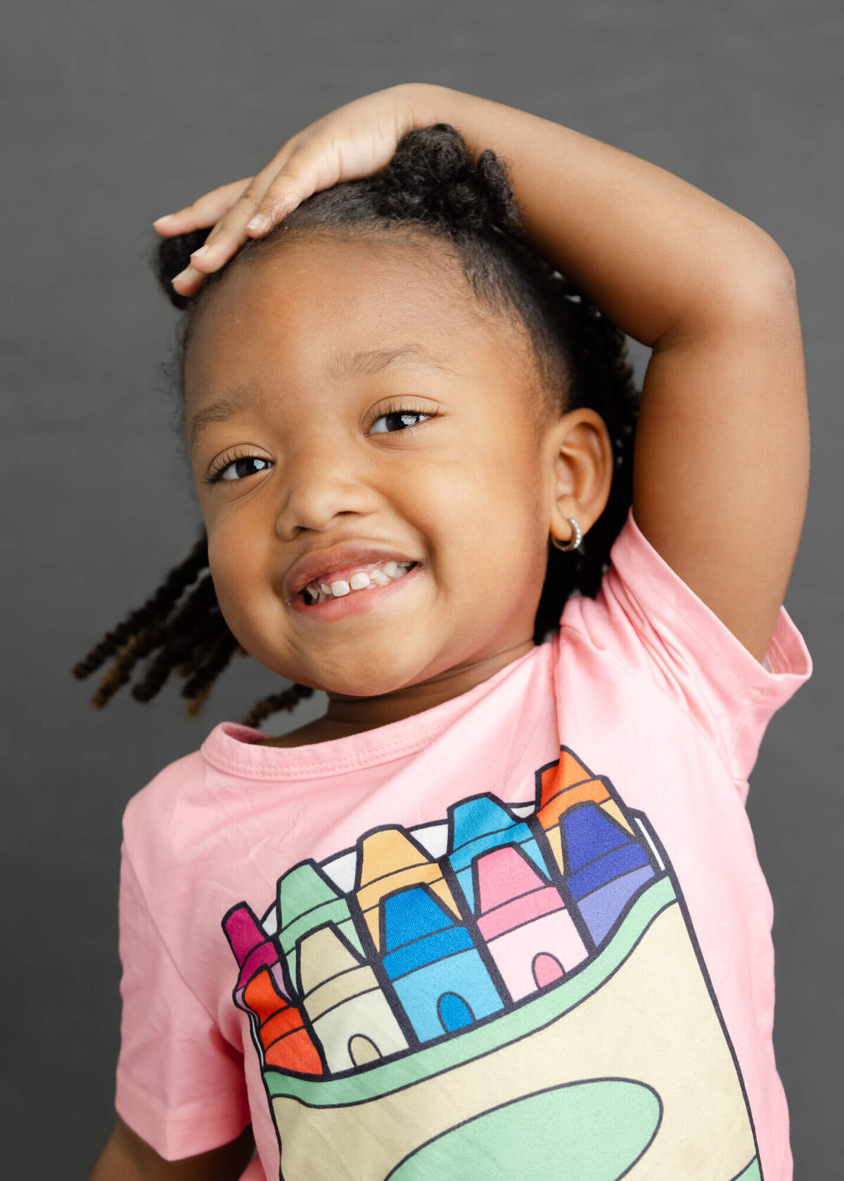 Cute African American preschooler in a pink crayon shirt poses with her hand on her head for her preschool Fine Art Portrait