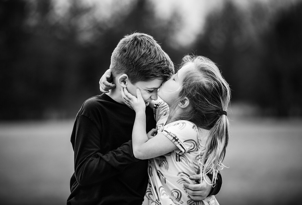 black and white image of little sister kissing her older brother on the forehead