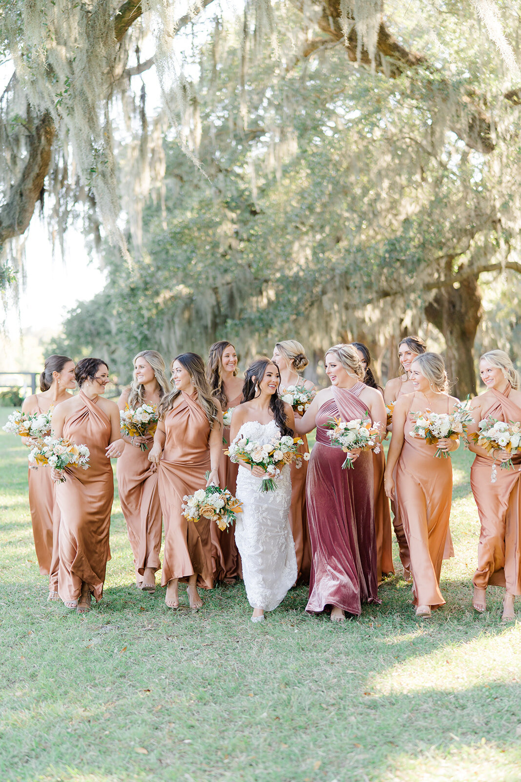 Jewel-toned bridesmaids dresses. Bride walking with bridesmaids on the lawn under spanish moss and live oaks. Fall wedding at Boone Hall.
