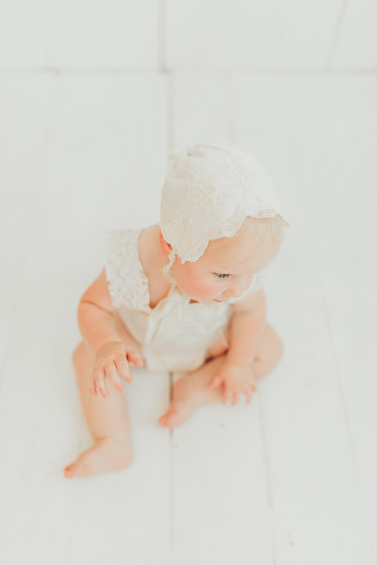 Baby girl wearing white bonnet and white romper on studio location in Houston Texas.