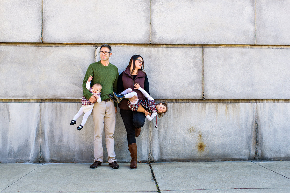 A family portrait in philly of two parents holding their two kids upside down.