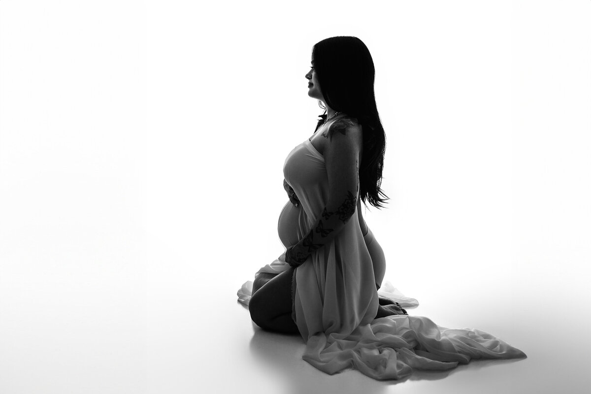 black and white studio image of a charlotte mother draped in a white silk wrap on a white backlit background