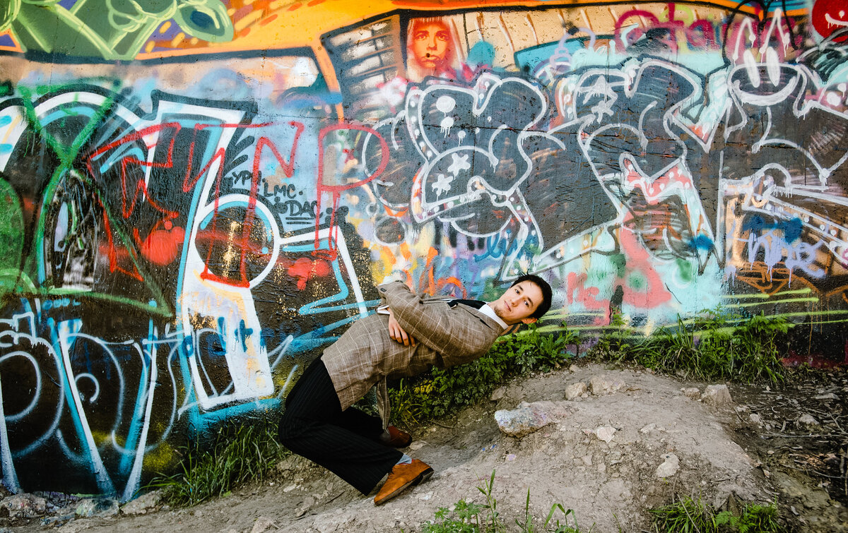 A person leaning back while standing in front of a wall covered in graffiti
