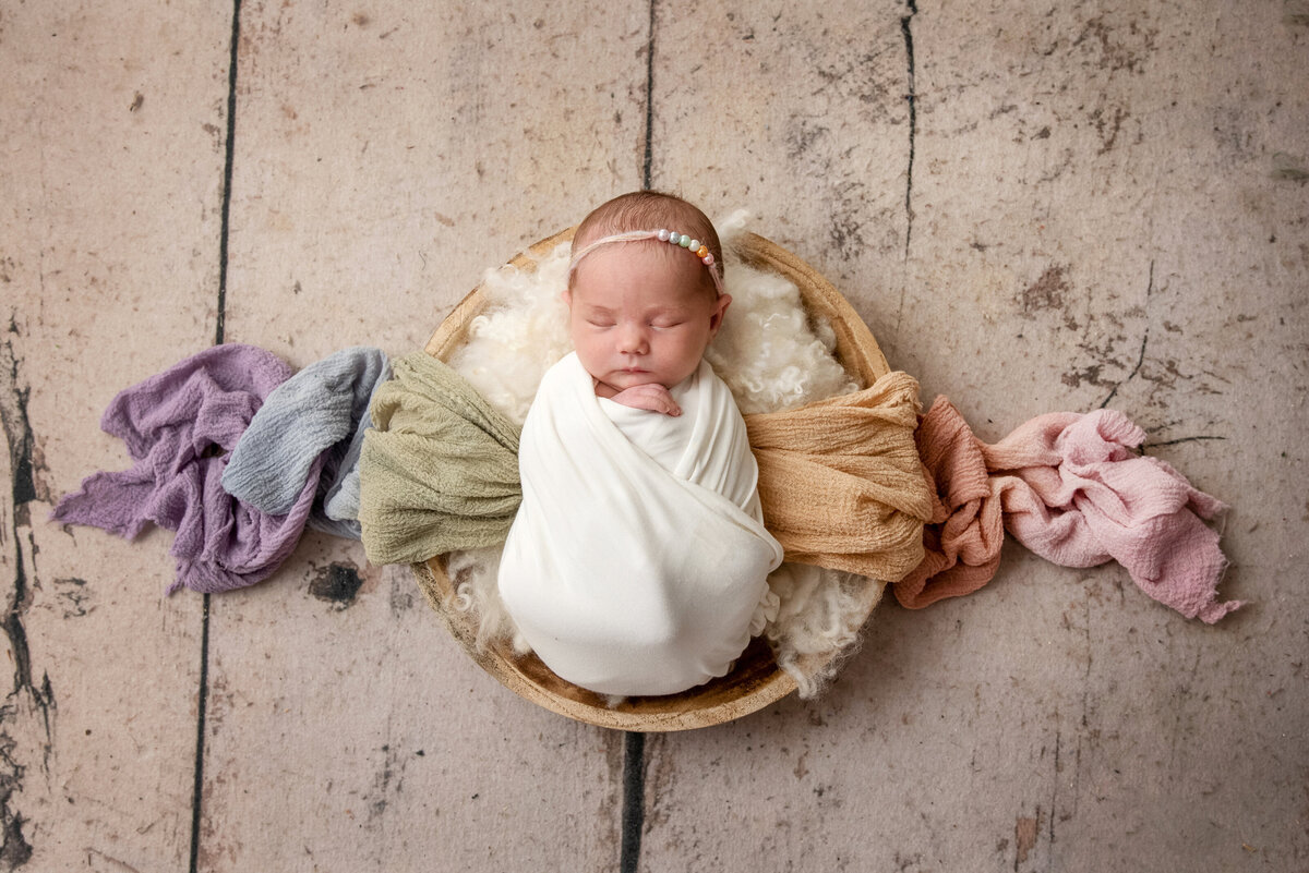 st-louis-newborn-photographer-baby-swaddled-in-white-in-basket-with-flowing-out-rainbow-pastel-fabrics