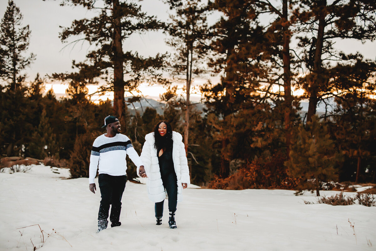 colorado couple hold hands while walking in the snow for engagement session at mt falcon colorado