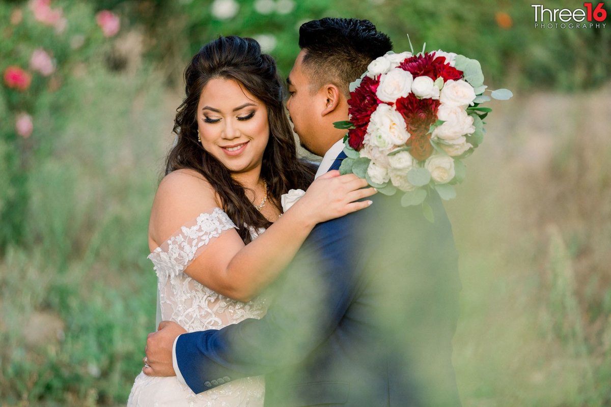 Groom whispers into his Bride's ear during photo session in the fields of shrubbery