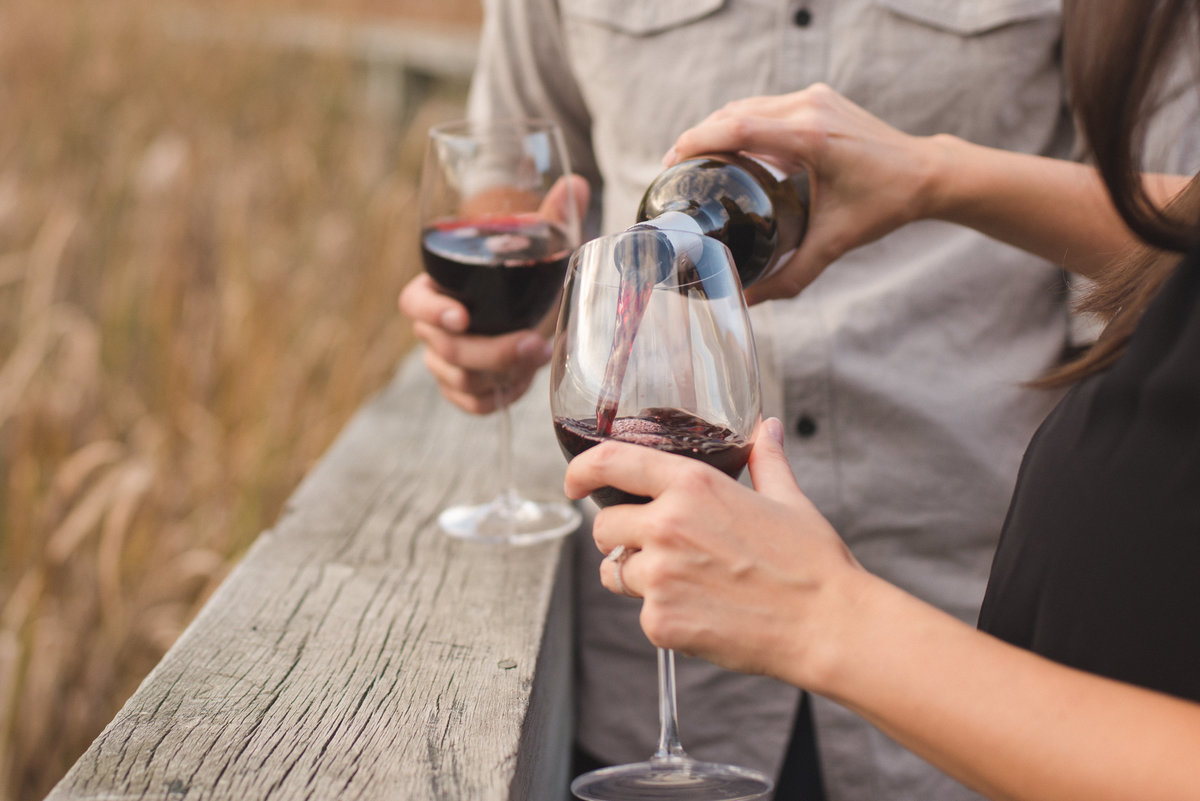 Couple pouring each other a glass of red wine during engagement session