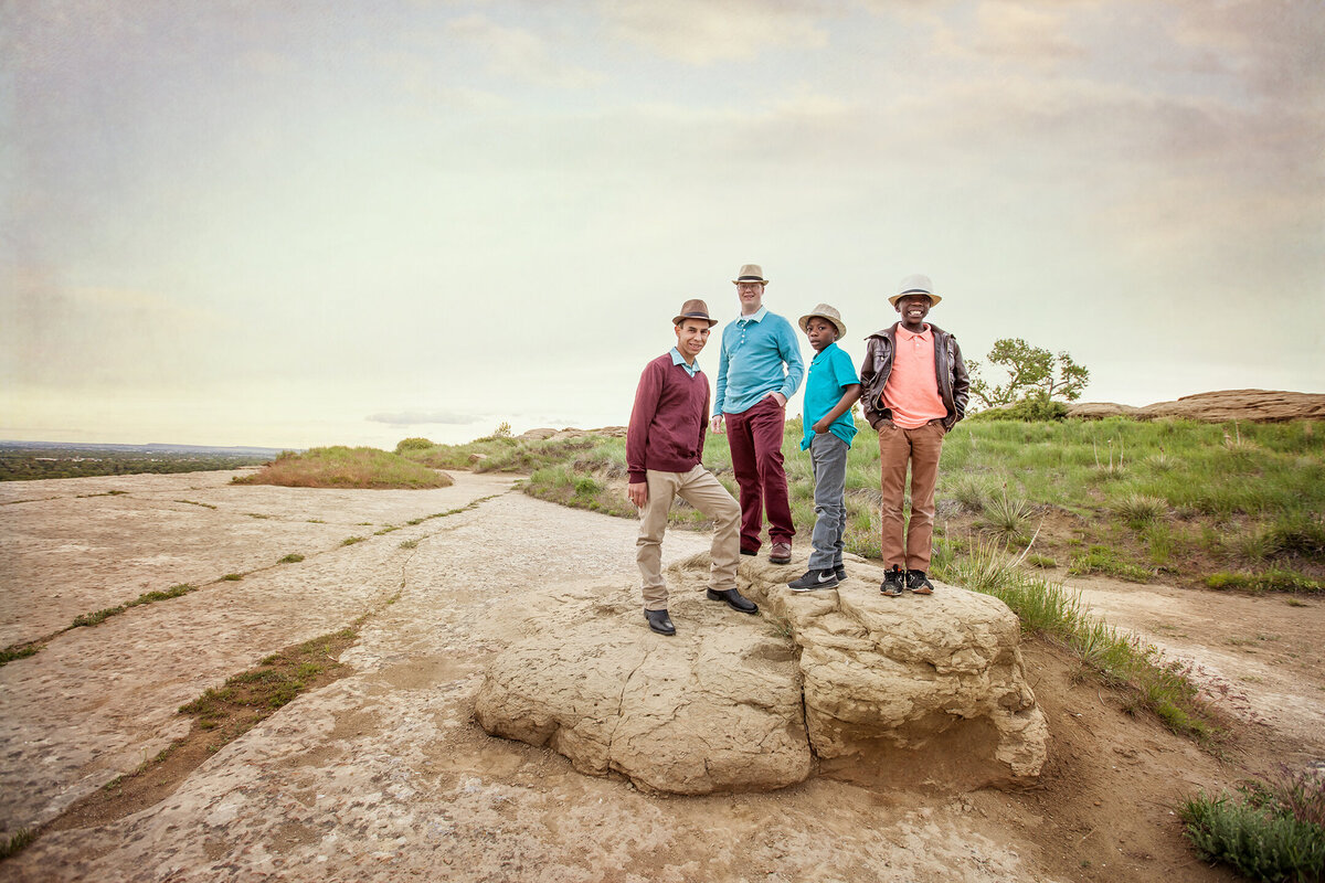 brothers standing on large sandstone rock with leading lines near sunset, teal, maroon, pink, gray and brown wearing hats and swords park next to airport in billings montana.