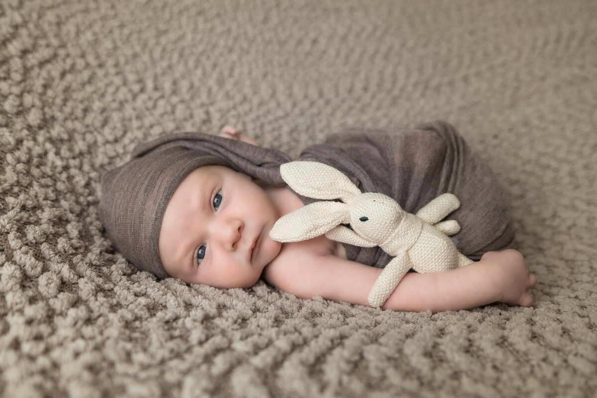 Newborn Photographer, a baby sleeps on woven quilt holding a knit bunny