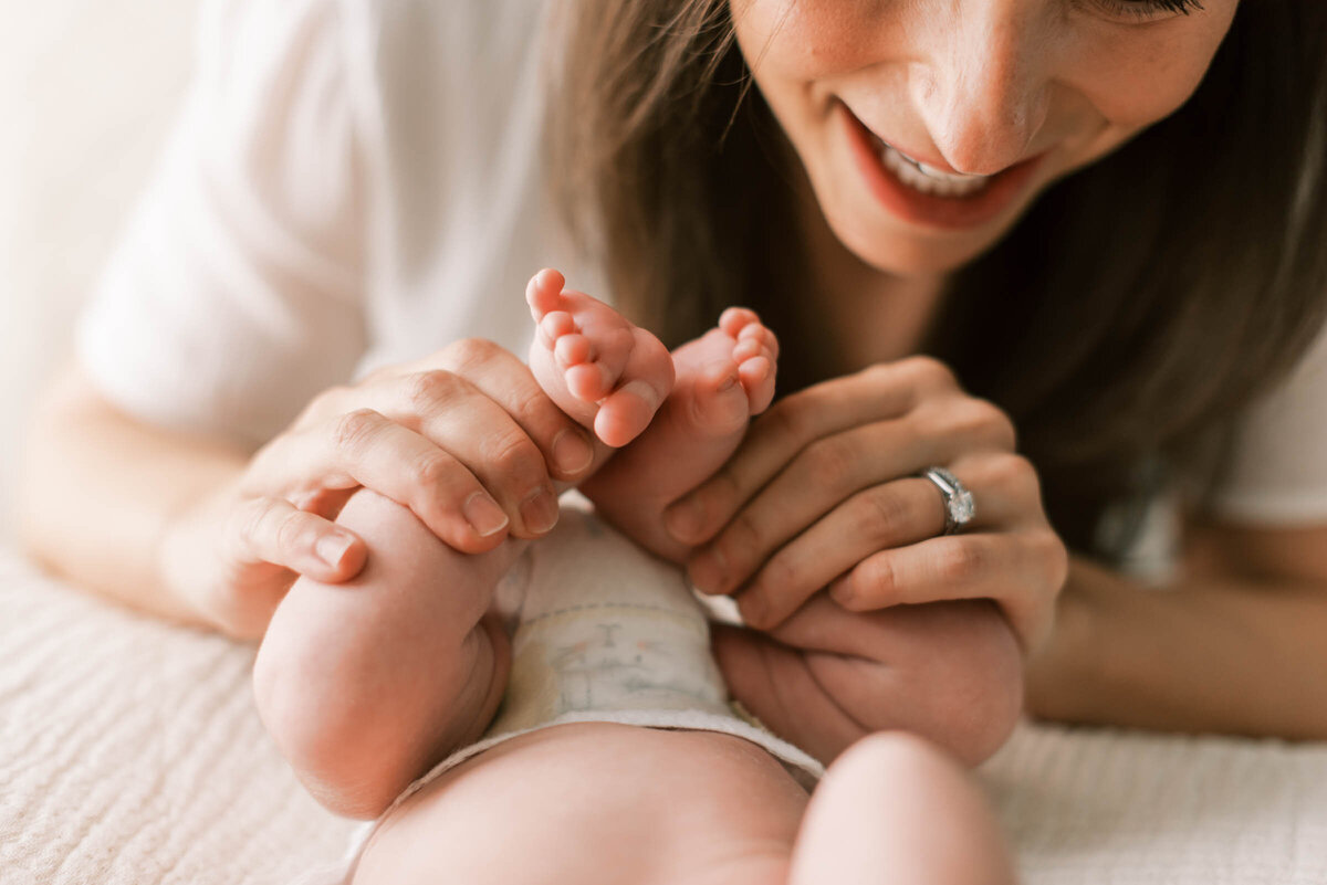 A mother holds and kisses the toes of her newborn baby