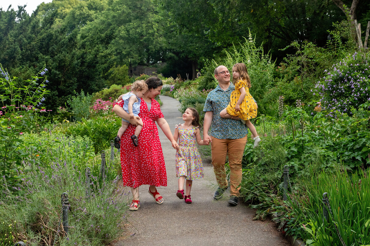 a family of five in brightly colored outfits walk through Fort Tryon Park in New York City family sleeping newborn baby boyA black family of four has a tickle fight on a patchwork quilt Brooklyn family photographer Milestone Images