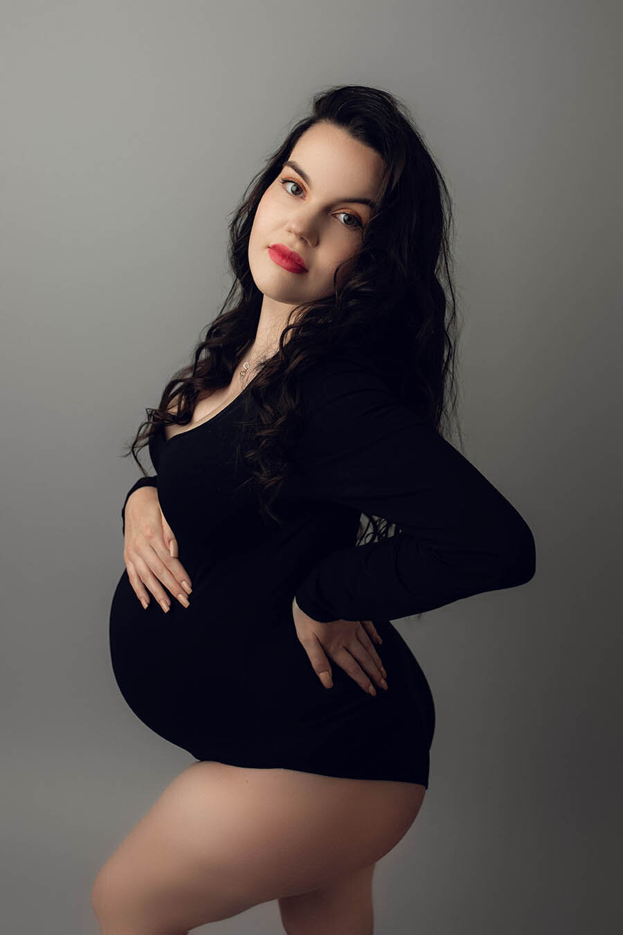 a pregnant woman posed to the side with her hand on her back and the other hand on her bump