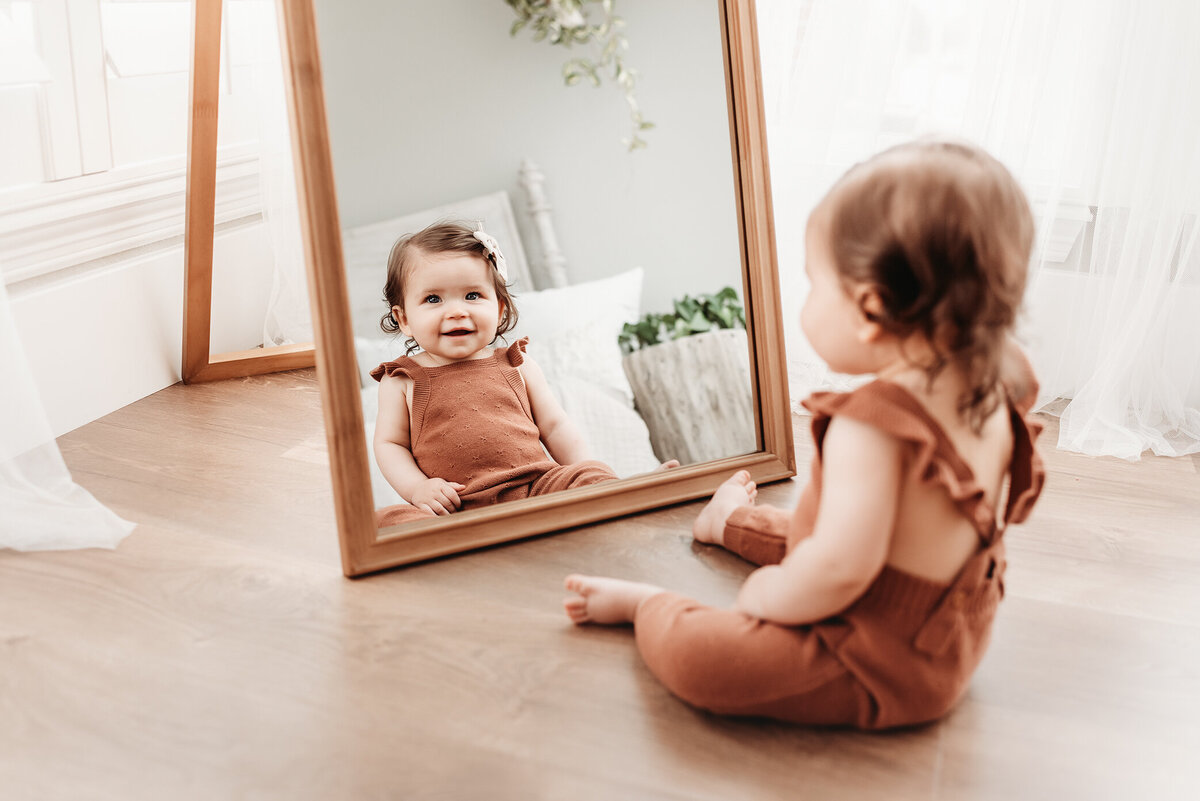 baby girl sitting at mirror looking at herself