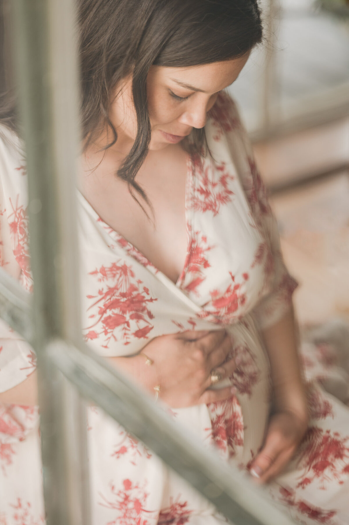 Image shot through a window by San Antonio maternity photographer Cassey Golden of an expecting mom gazing at her bump.