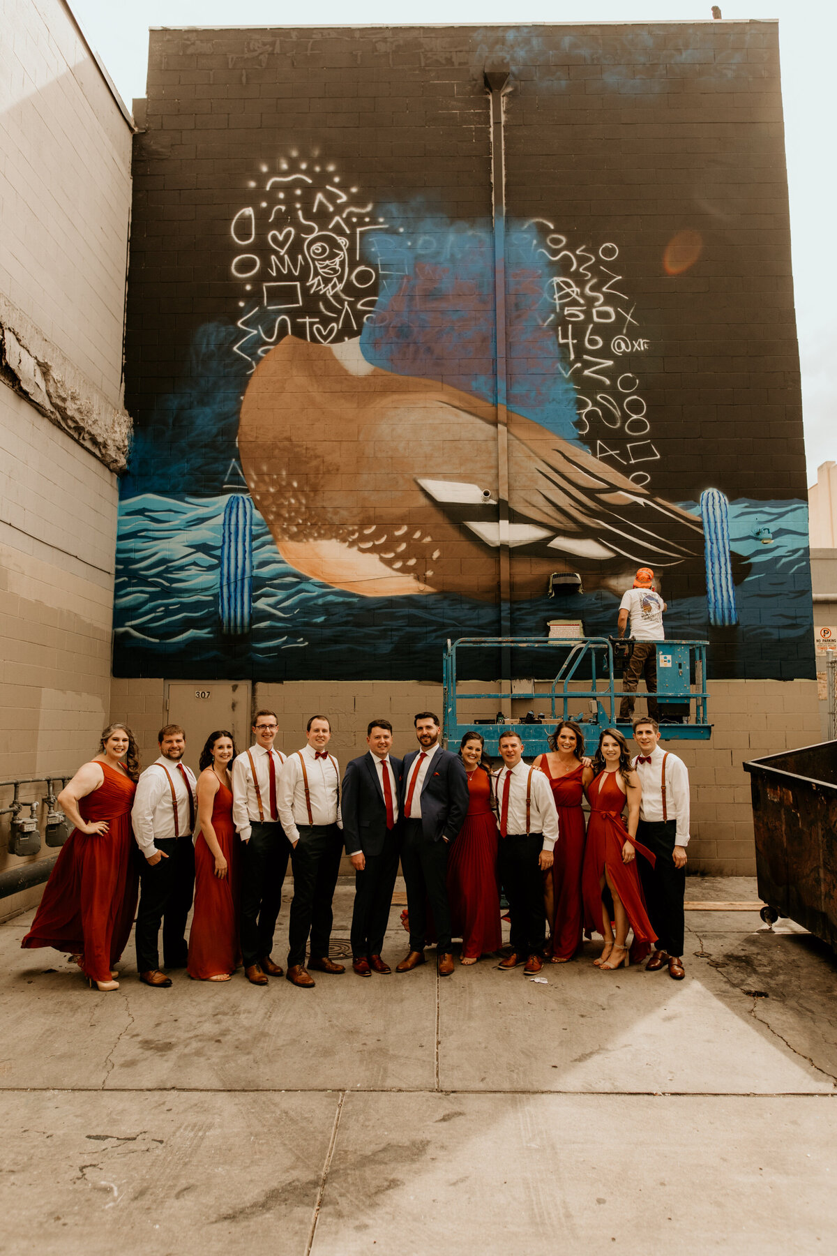 same sex couple standing in front of wall art with their wedding party in Albuquerque