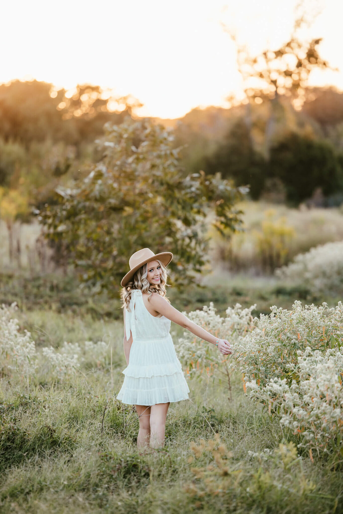 senior photo of girl in short white dress in open field at sunset