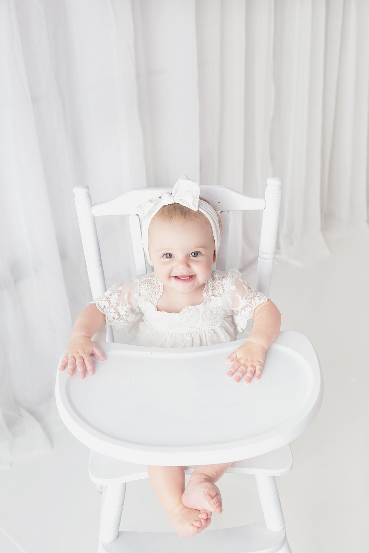 Little girl sitting in white high chair  during first birthday photoshoot in Brentwood Tennessee photography studio