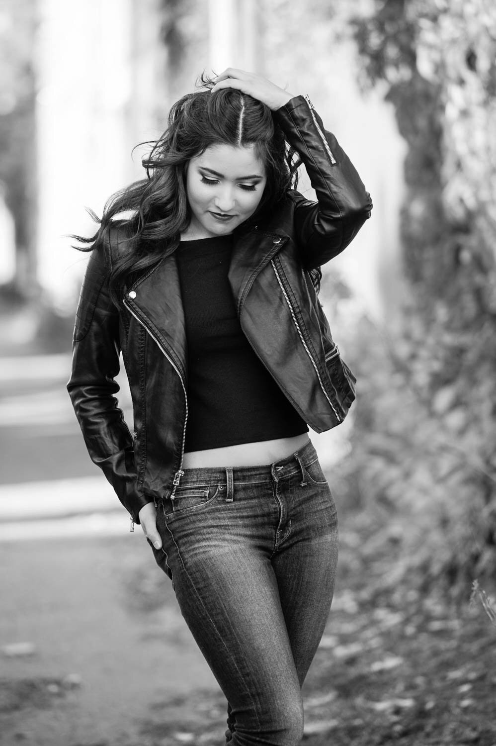 senior photo of girl wearing leather jacket and jeans in nature