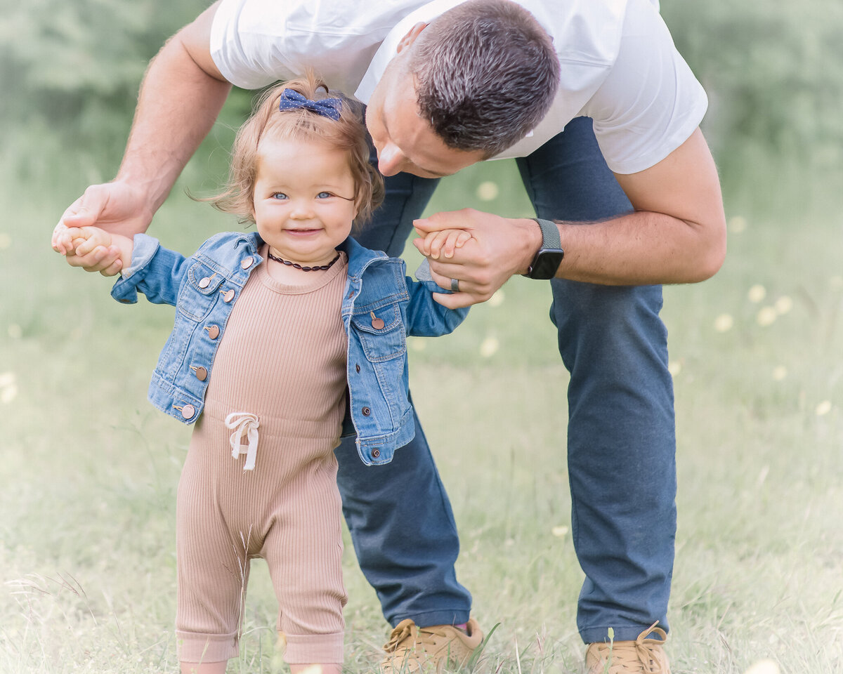 adorable toddler standing with dad holding her hands outdoors