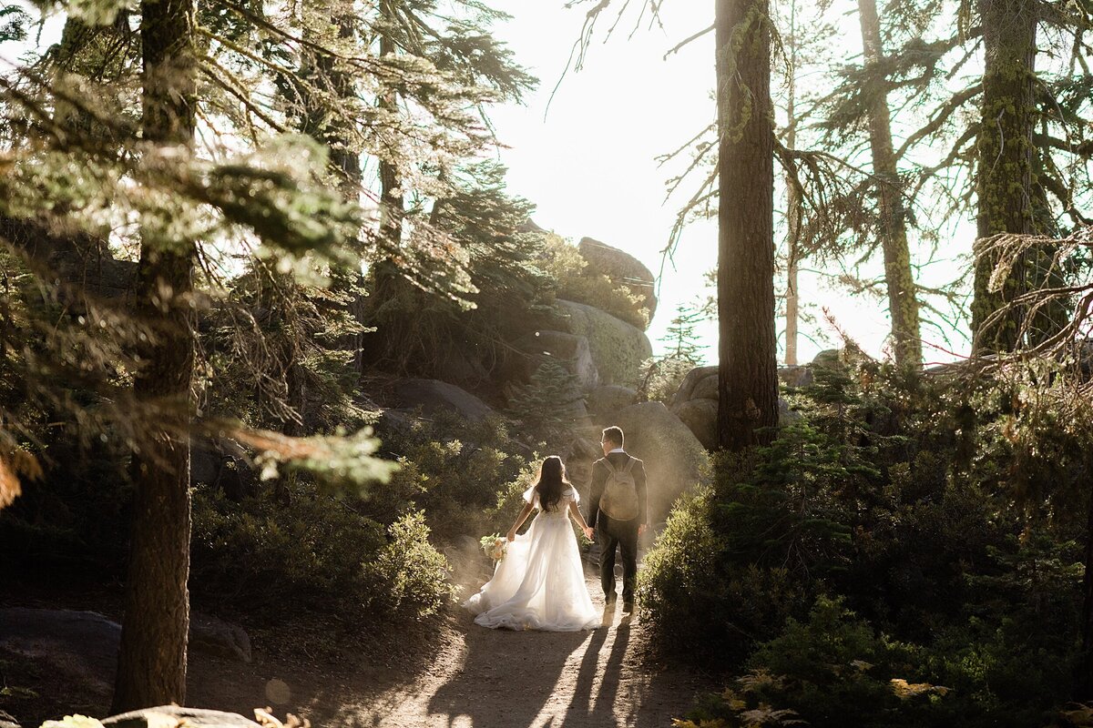 The bride and groom walk in a forest with the sun shining through during their Yosemite hiking elopement