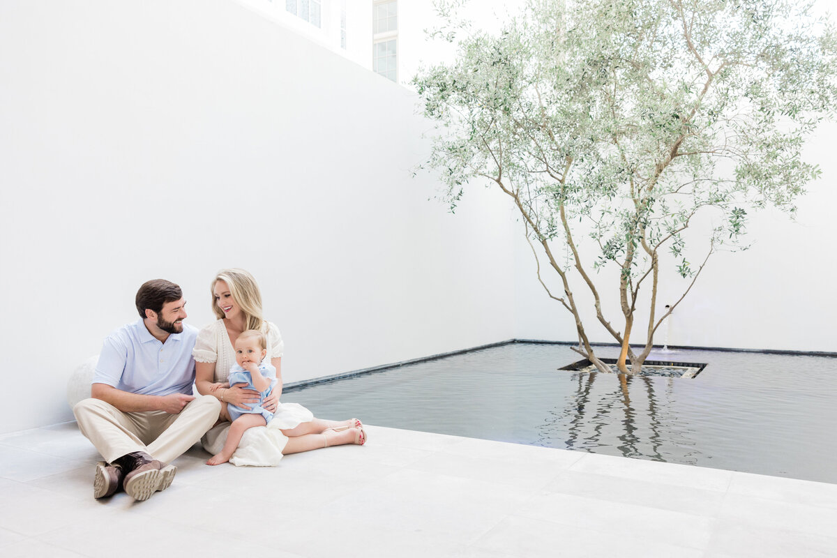 Two parents sitting on the ground with a baby in their lap at a home courtyard in Alys Beach Florida.