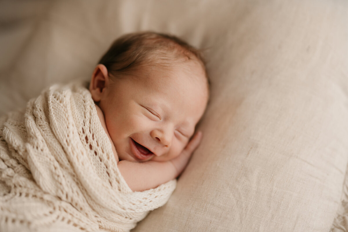 Photo of a newborn baby during a natural newborn photography shoot. The baby is asleep and smiling