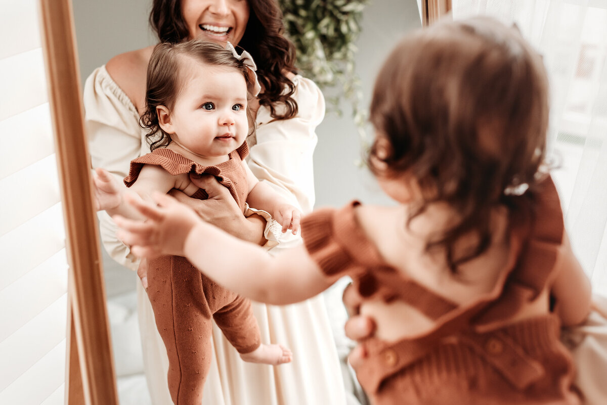 mom holding baby girl near mirror to look at reflection