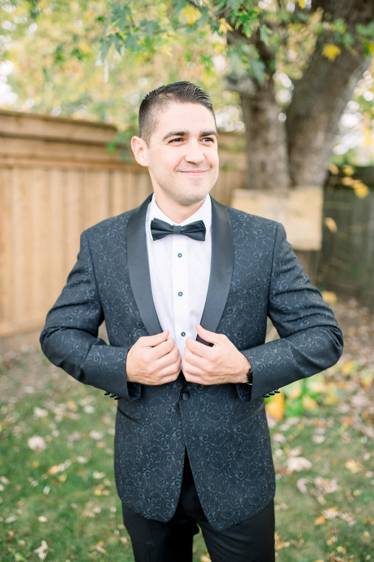 Groom adjusts jacket while smiling. Captured by Niagara wedding photographer
