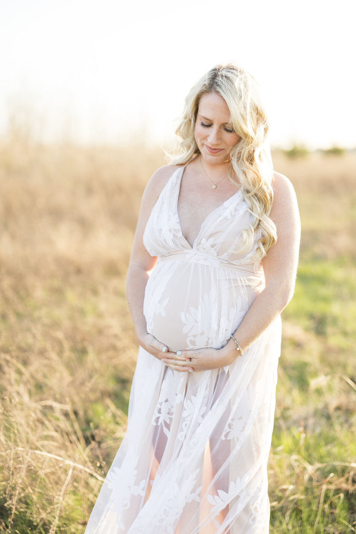 Pregnant woman standing in a field holding her belly