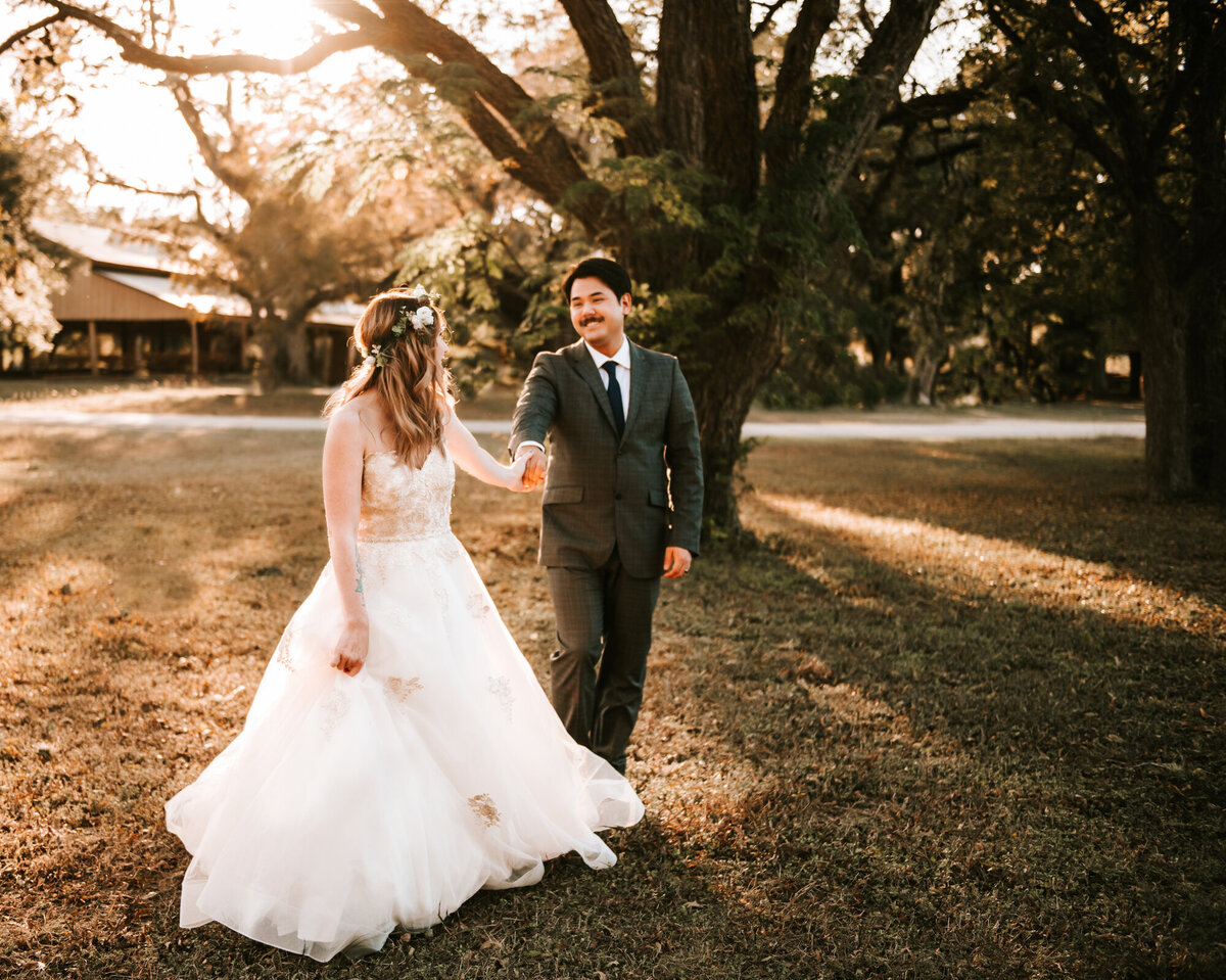 Couples Photography, Woman in a wedding dress holds hands with man in a blue suit and walks towards the camera in the sun.