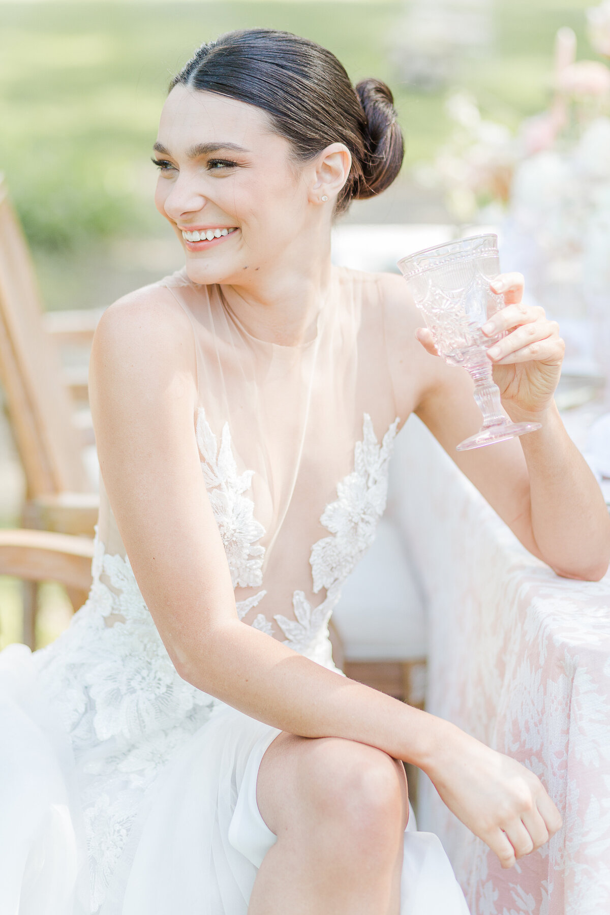 A bride is captured casually sitting at a table for a candid portrait. The bride is sitting with her leg crossed and she is looking over her shoulder smiling