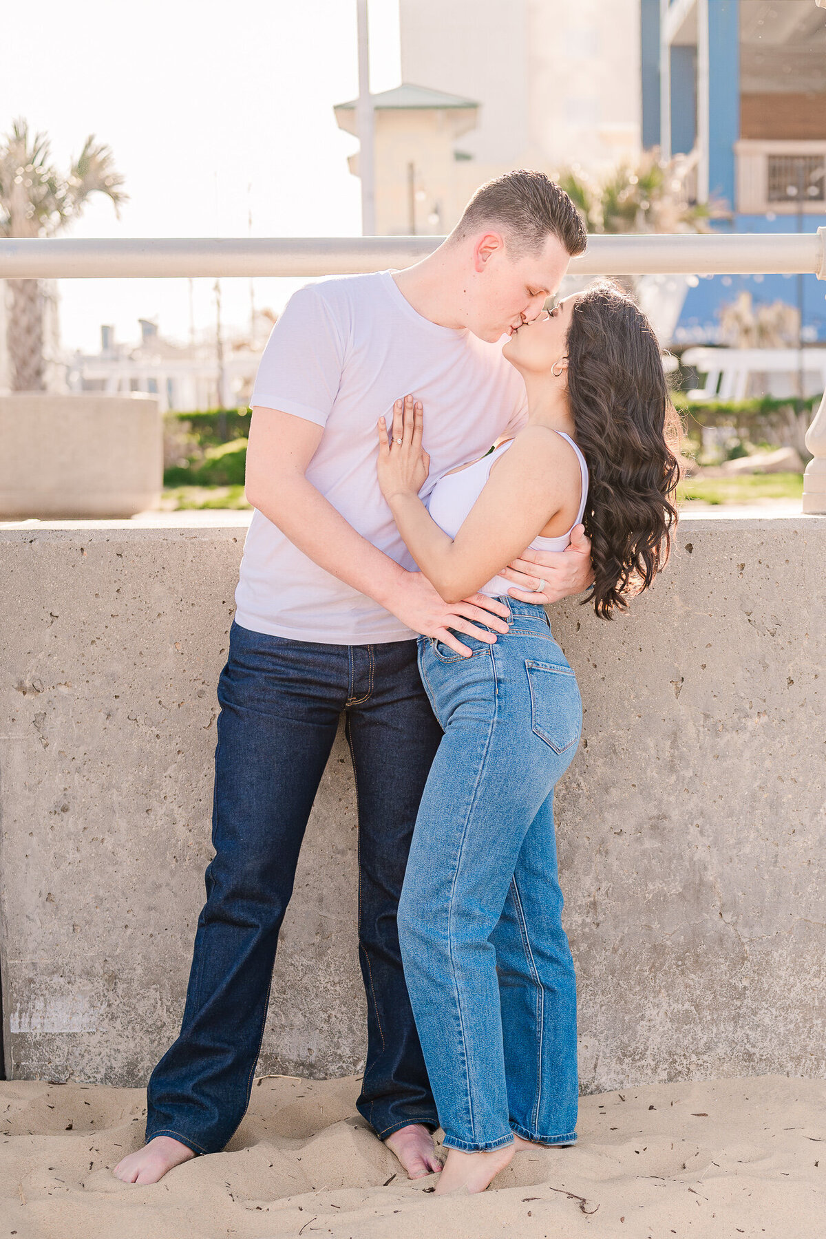 A loving couple in jeans and white shirts kissing at sunset by Wilmington wedding photographer, JoLynn Photography