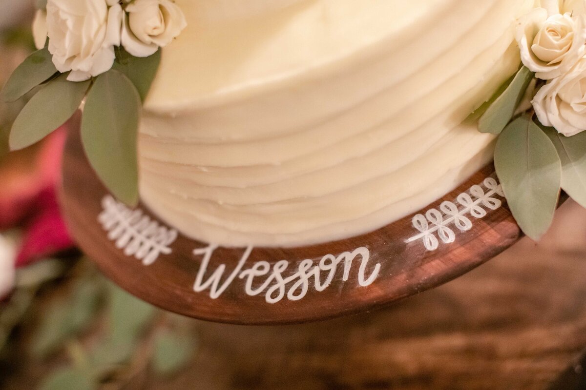 last name written in chalk marker on wooden cake pedestal at Morgan creek Barn wedding in Dripping Springs Texas