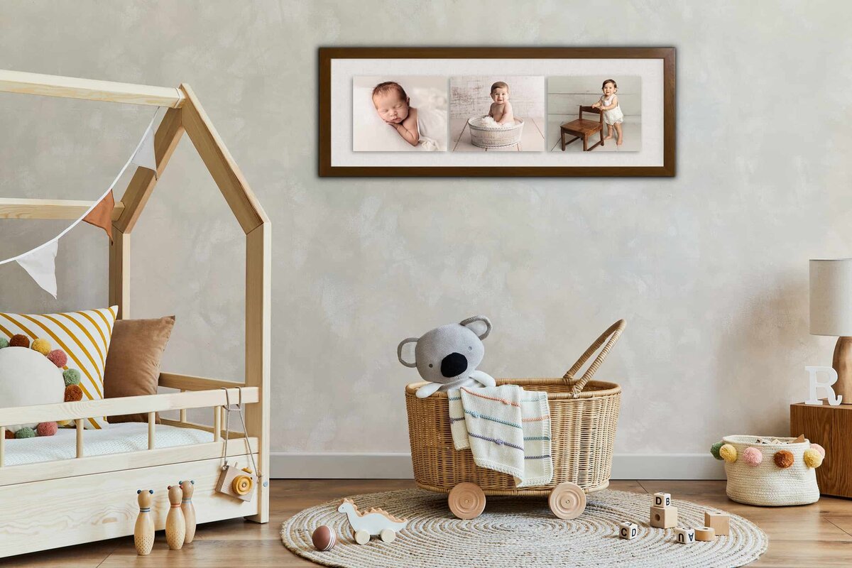 Three fine art baby photographs hang framed on a wall of a nursery and play room with wooden toys