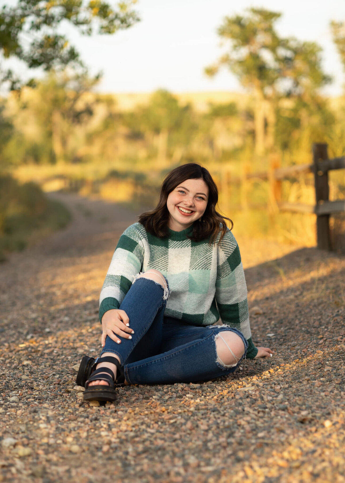 teenage girl wearing a green sweater and jeans sitting on a  rocky trail