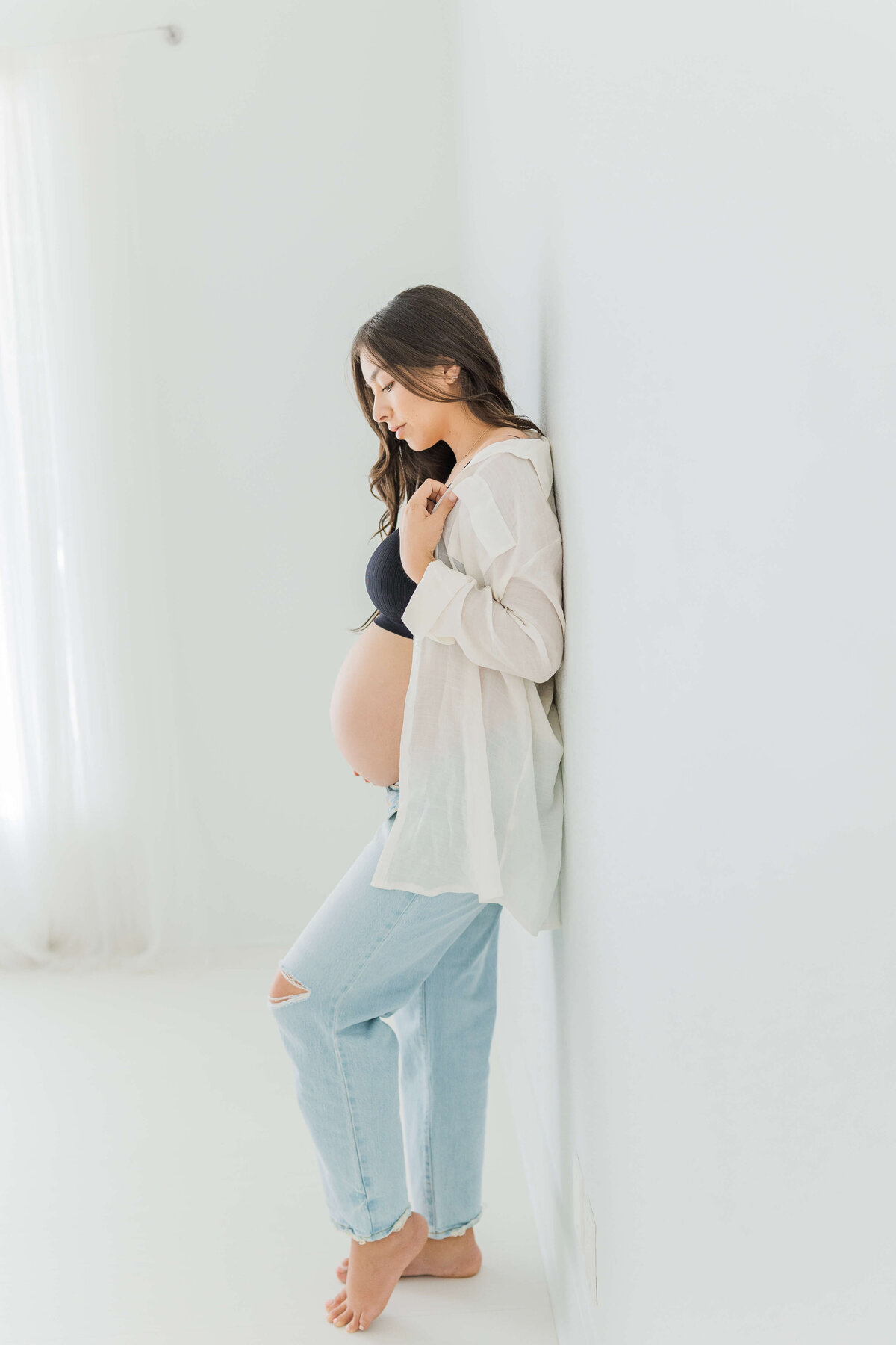 Mother standing against wall while looking down at her pregnant belly
