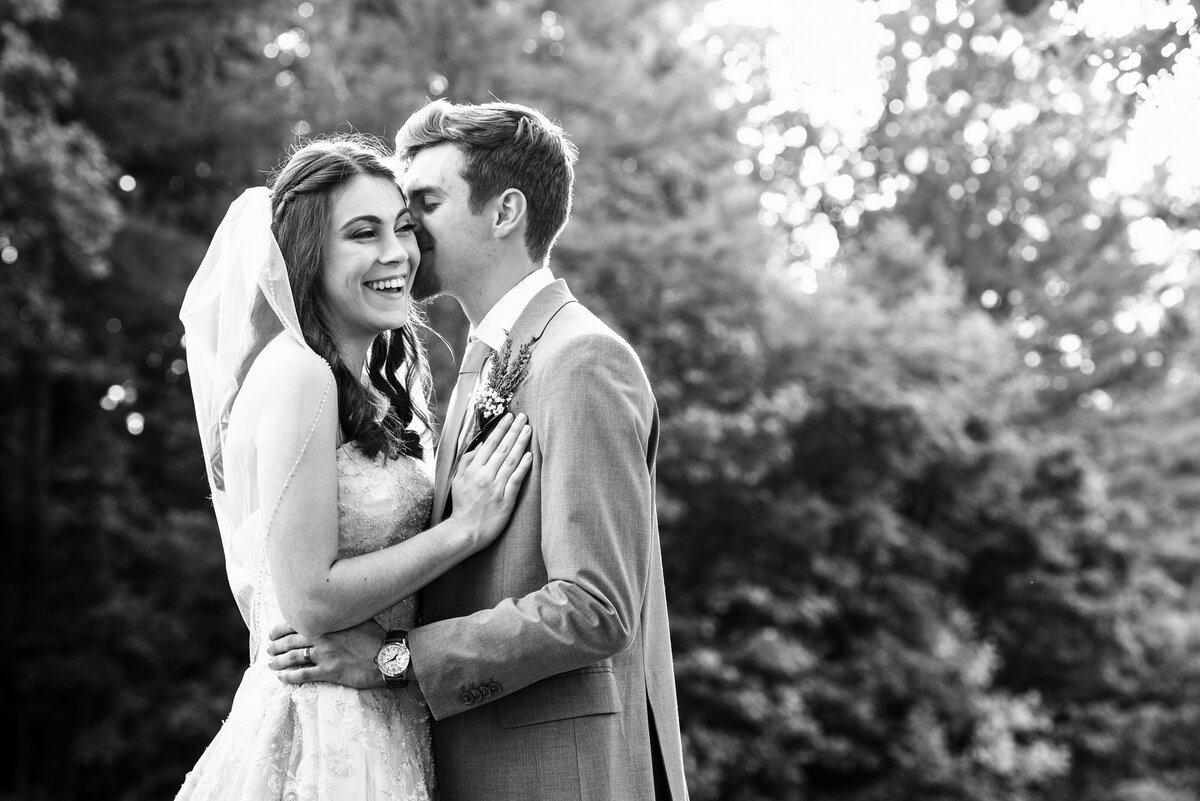 Black-and-white-photograph-of-a-bride-and-groom-outdoors-bride-laughing-as-groom-whispers-in-her-ear