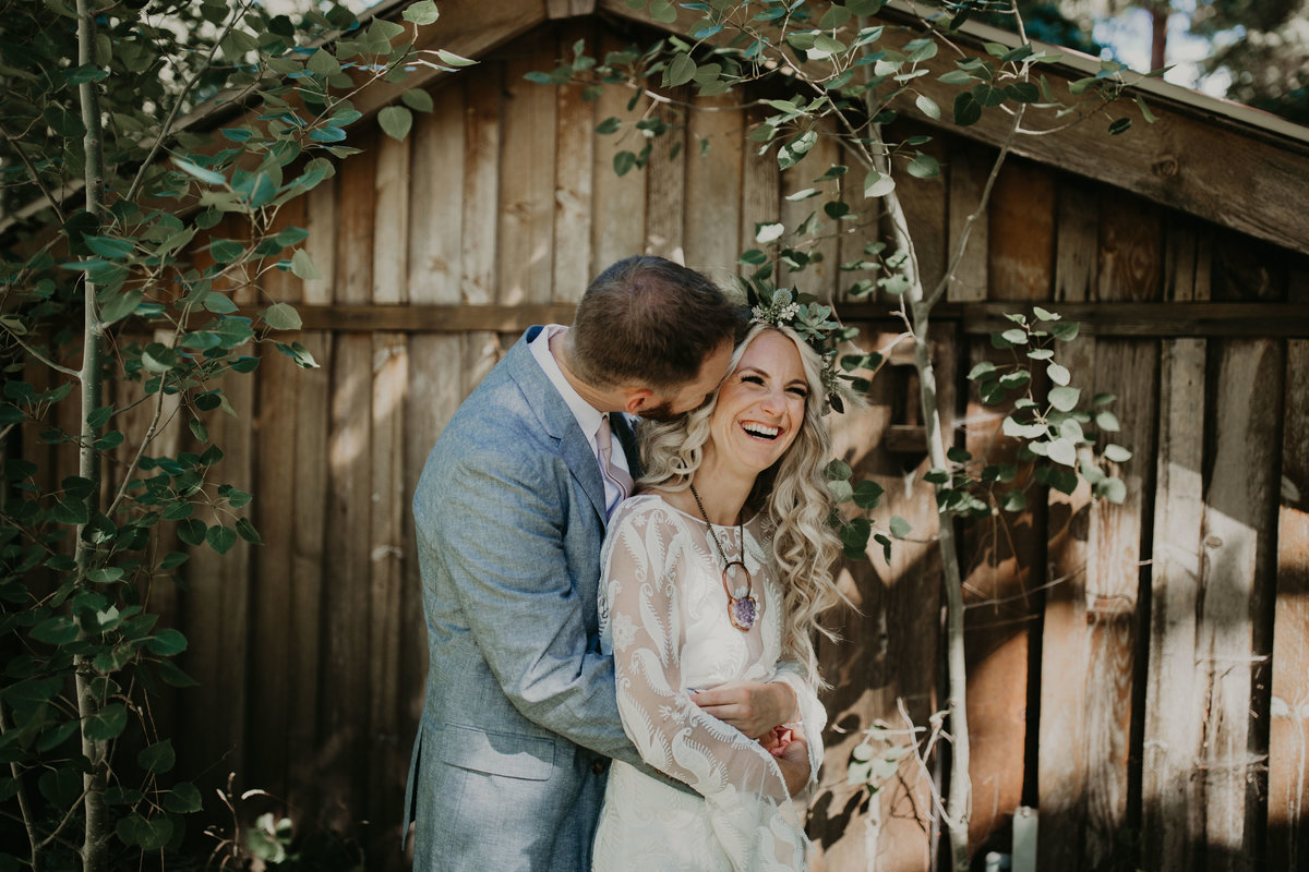 Groom kisses brides cheek while she smiles and laughs on their wedding day at Mountain Spring Lodge in Washington