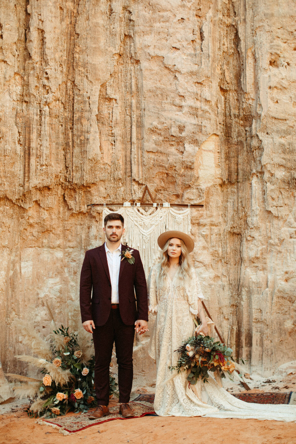 Eloping bride and groom standing in front of canyon wall at the ceremony site with vintage rugs and macrame arch decor