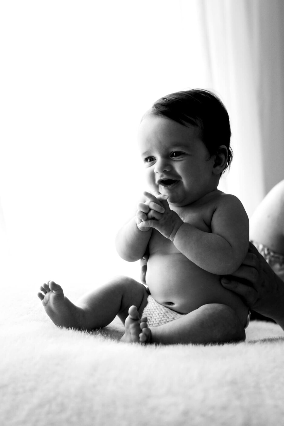 Black and white portrait of a baby girl sitting on a bean bag and smiling.