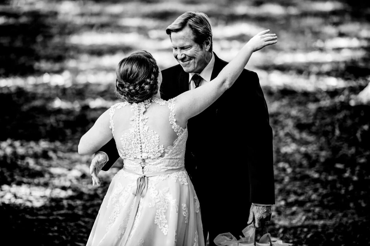 A groom, seen from the back, tenderly holds his bride’s hand, both looking into the distance, in a black and white outdoor setting that evokes a sense of serenity.