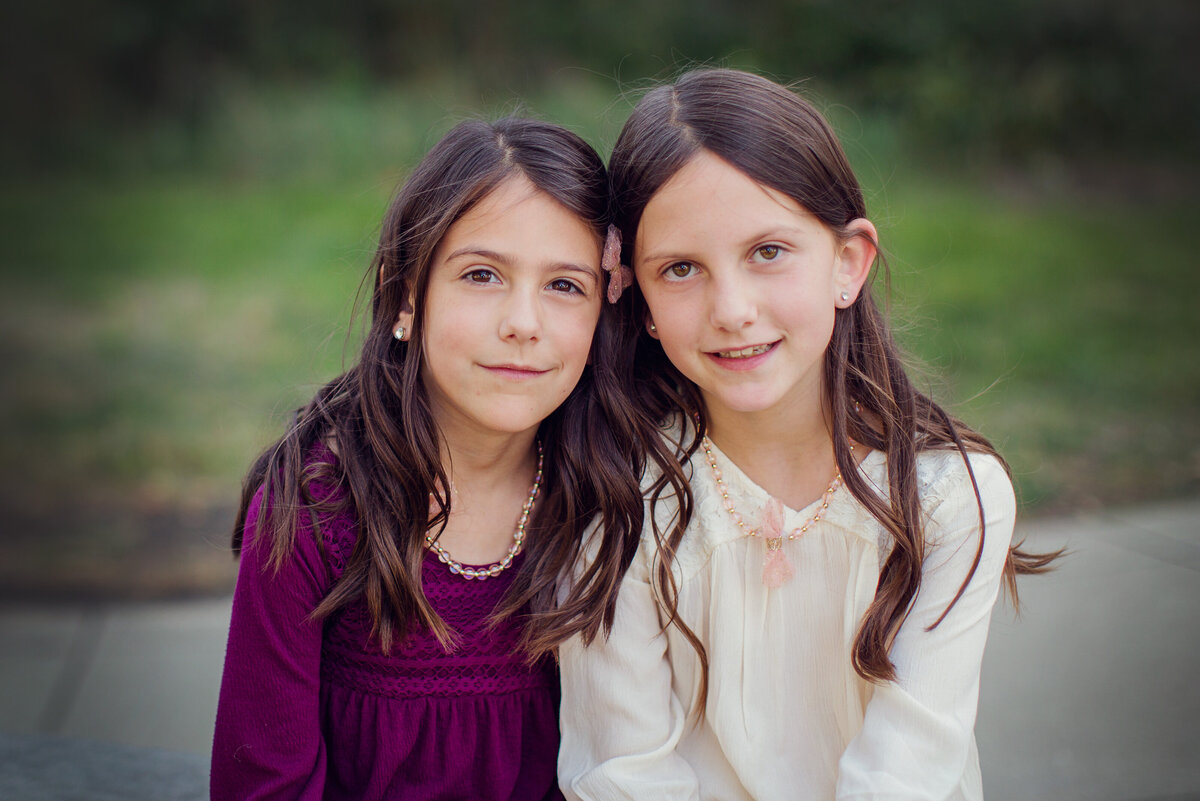 Sisters, both with long, dark hair, are smiling at the camera.