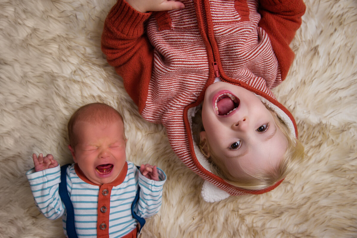 Newborn crying at newborn session with excited sibling