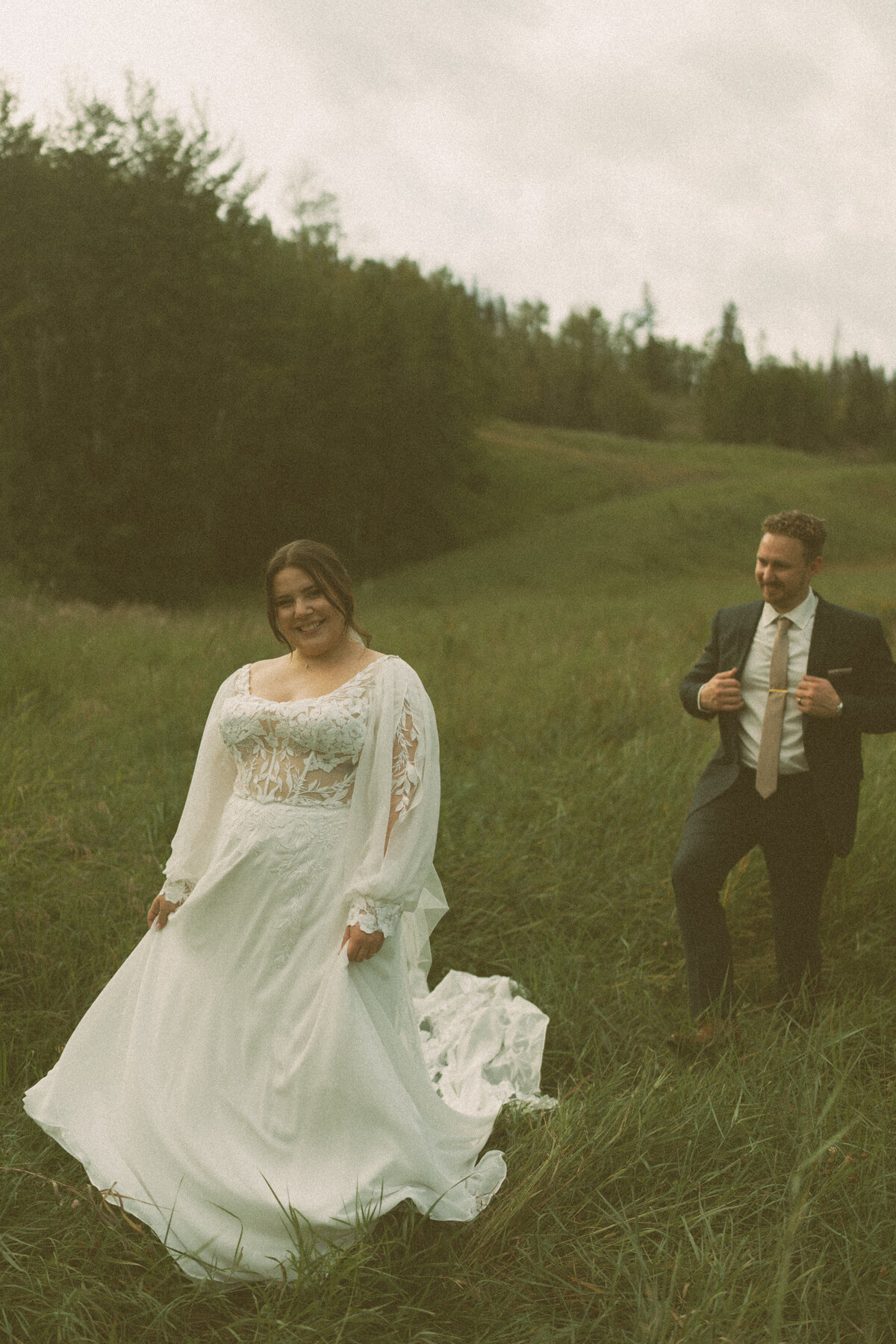 storytelling summer wedding photo of bride smiling at camera while groom admires his bride from a distance